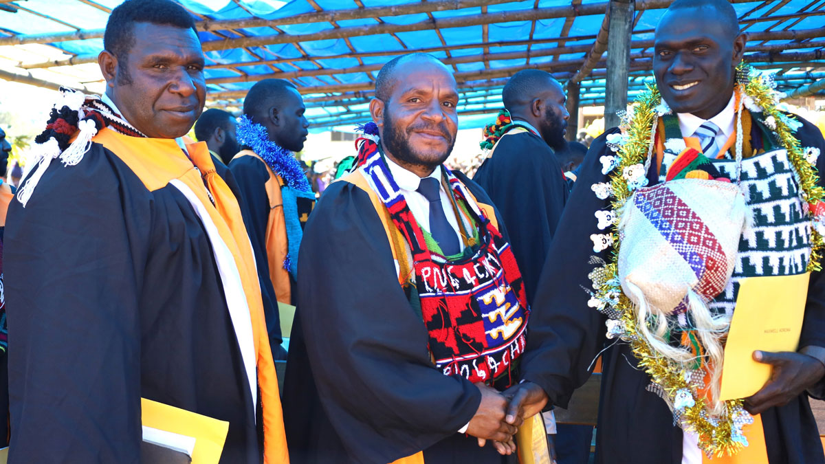 Three graduates of Omaura School of Ministry stand with their robes and certificates.